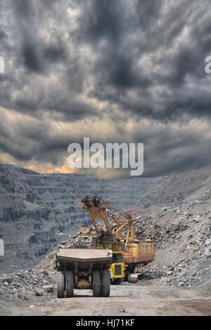 Schwere Bergbau Muldenkipper sind mit Eisenerz auf den Tagebau mit stürmischen Wolken im Hintergrund geladen wird Stockfoto