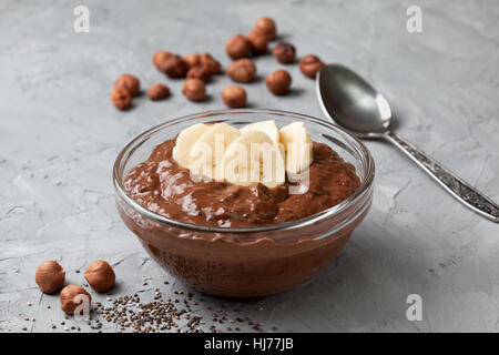 Schokolade Haselnuss Chia Pudding mit Banane in eine Glasschüssel auf grauem Beton Hintergrund Stockfoto