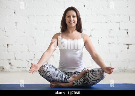 Junge attraktive Frau im Ardha Padmasana Pose, weiße Studio bac Stockfoto