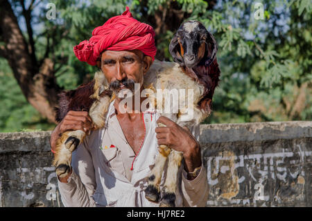 Mann mit rotem Turban mit Ziege auf seinen Schultern. Stockfoto