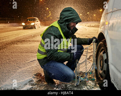 Mann mit Warnweste Anwendung Schneeketten auf schneebedeckte Straße, Wattens, Tirol, Österreich Stockfoto