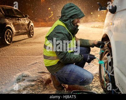 Mann mit Warnweste Anwendung Schneeketten auf schneebedeckte Straße, Wattens, Tirol, Österreich Stockfoto