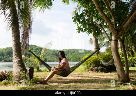 Asiatische Frauen sitzen und relaxen am Möbel Hängematte hängen zwischen den Palmen im Garten des Resort vor dem Strand und tropischen Meerwasser bei Ko Yao N Stockfoto