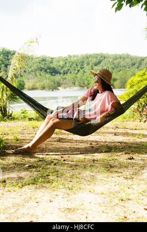 Asiatische Frauen sitzen und relaxen am Möbel Hängematte hängen zwischen den Palmen im Garten des Resort vor dem Strand und tropischen Meerwasser bei Ko Yao N Stockfoto