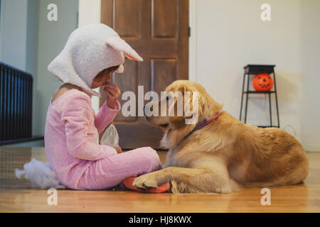 Mädchen im Bunny-Kostüm Halloween Süßigkeiten mit Golden Retriever Hund teilen Stockfoto