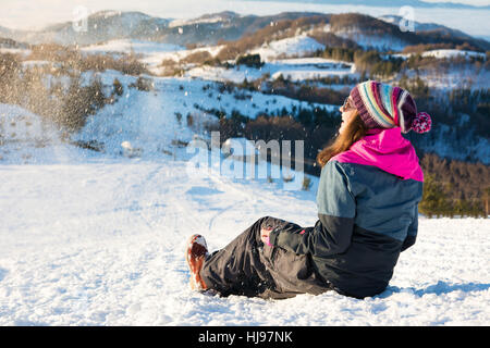 Glückliches Mädchen sitzen im Schnee auf dem Berg Stockfoto