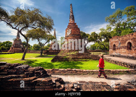 Tourist-Frau im roten Kostüm, Blick auf alten verfallenen Stupas in Ayutthaya Historical Park, Thailand Stockfoto