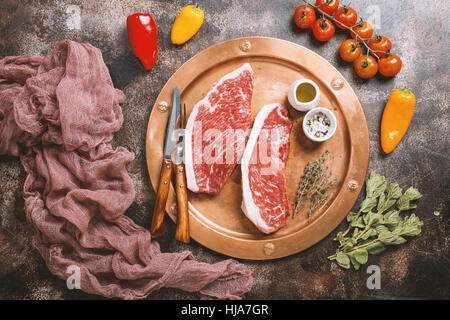 Frisches rohes Prime Black Angus Rindfleisch strip Steaks auf Metallplatte über rustikale Beton dunkel, Ansicht von oben. Zutaten für die Herstellung von gesunden Abendessen eingestellt Stockfoto