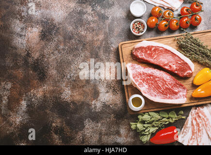 Frisches rohes Prime Black Angus Rindfleisch strip Steaks auf Schneidebrett über rustikale Beton dunkel, Ansicht von oben. Zutaten für die Herstellung von gesunden Dinn eingestellt Stockfoto