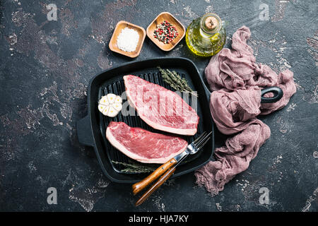 Frische rohe Prime Black Angus Rindfleisch Streifen Steaks auf Grill Pfanne über rustikale Beton dunkel, Ansicht von oben. Zutaten einstellen für die Herstellung von gesunden Abendessen Stockfoto