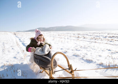 Niedliche kleine Mädchen draußen in der Natur Winter auf Schlitten sitzend Stockfoto