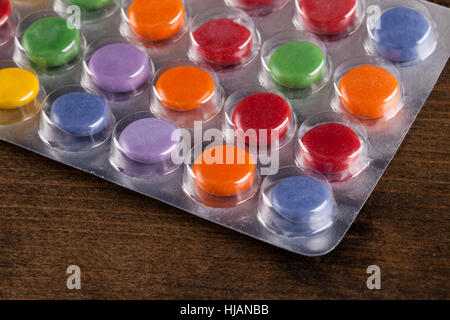 Pillen in einer Blase-Packung in einem Winkel betrachtet. Helle Farben und Runde Tabletten unter Kunststoff, auf einem Holztisch versiegelt Stockfoto