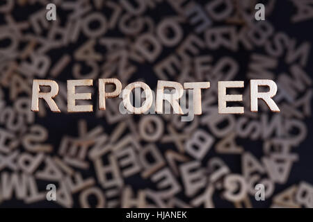 Reporter Holzbuchstaben Holz schwebt über zufällige Buchstaben unten außerhalb des Fokus auf einem schwarzen Hintergrund gegründet Stockfoto