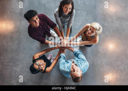 Gruppe von glücklichen jungen Studenten zeigen Einheit. Draufsicht der multiethnische Gruppe junger Leute setzen ihre Hände zusammen. Junge Studenten stehen in einem Stockfoto