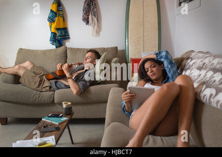 Junges paar entspannende auf Sofa mit digital-Tablette und Gitarre spielen Stockfoto