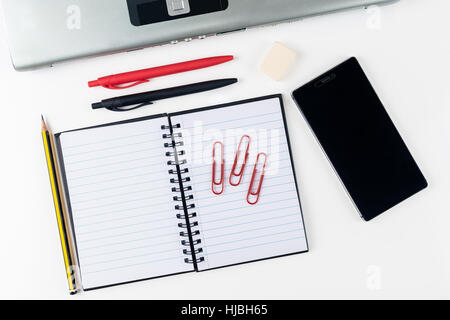 Office-Arbeitsbereich auf weißem Hintergrund mit Smartphone und Laptop. Notebook-Rohling mit Bleistift, Feder und Clips. Platz für Text oder das Bild zu kopieren. Stockfoto