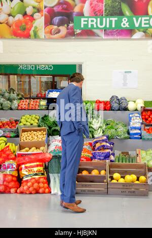 Mann im blauen Anzug suchen im Bereich Obst und Gemüse essen Großhändler. Stockfoto