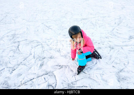 Kind Mädchen sitzt auf dem Eis nach einem Sturz im verschneiten Park während der Winterferien Stockfoto