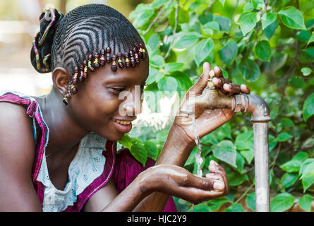 Glücklich afrikanischen Schülerin genießen Sie sauberes Wasser aus einem Hahn in Bamako, Mali Stockfoto