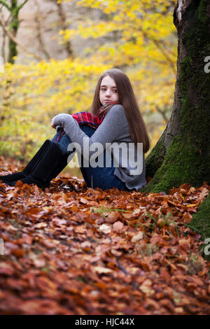 Hübsche junges Mädchen sitzen auf getrocknete Blätter in einem Wald im Herbst Stockfoto