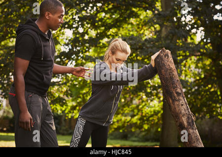 Junge Frau mit Personaltrainer Aufhebung Baumstamm im park Stockfoto