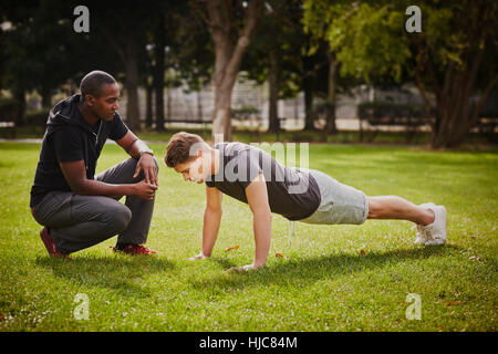 Persönlicher Trainer unterrichten jungen Mann tun Push ups im Park Stockfoto