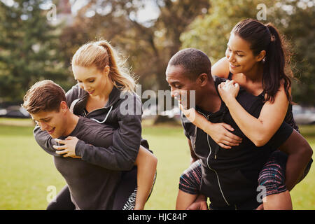 Männer und Frauen, die Spaß im Park, mit Huckepack-Rennen training Stockfoto