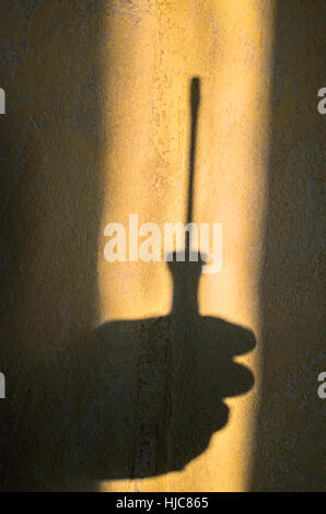 Hand mit Schraubendreher auf dem gelb und schwarz Grunge konkreten Hintergrund. Hand-Werkzeuge im Einsatz. Hand mit Werkzeugen arbeiten. Flachen Stil. Hardware-Tools. Stockfoto