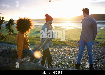 Drei Erwachsene Freunde Sonnenuntergang über Meer, während Treibholz sammeln Stockfoto