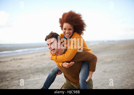 Paar am Strand Huckepack spielen Stockfoto