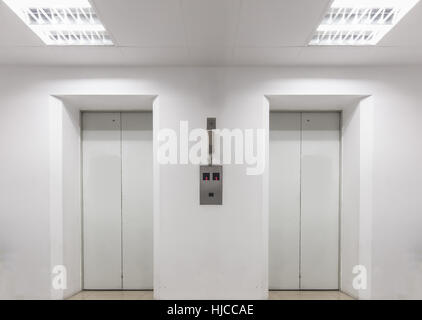 Zwei Aufzüge im inneren weißen Gebäude im ersten Stock mit Licht an Decke. Notruftelefon über Taste zwischen Aufzüge verbunden. Stockfoto