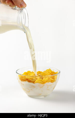 Milch Eingießen in Schüssel Cornflakes auf weißem Hintergrund Stockfoto