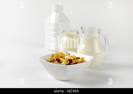 Schüssel mit Haferflocken mit Milch und Joghurt auf Wollweiß Hintergrund mit Schatten Glas Krug Stockfoto