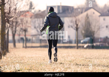 natürliche farbige Bild einer Frau, die läuft auf dem trockenen Rasen im Herbst oder Winter, übt sie für ihr tägliches workout Stockfoto