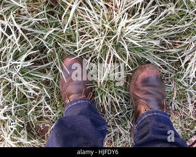 Erhöhte Ansicht der Person stehen in einem frostigen Feld. Braune Lederschuhe und blaue Jeans, Stockfoto