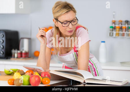 Reife Frau Kochbuch in der Küche auf der Suche nach Rezept lesen Stockfoto