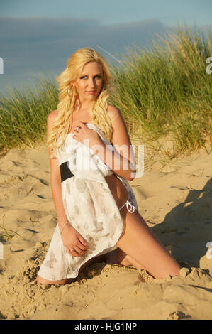 Schöne langhaarige blonde junge Frau in einem Sommerkleid am Strand. Stockfoto