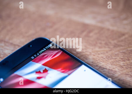 Smartphone auf hölzernen Hintergrund mit 4G Netzentgelt Zeichen 25 Prozent und Kanada-Flagge auf dem Bildschirm. Stockfoto