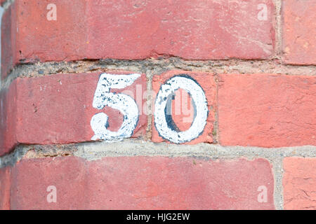 Haus Nr. 50 Zeichen weiß lackiert mit schwarzer Unterwolle auf roten Backsteinmauer Stockfoto