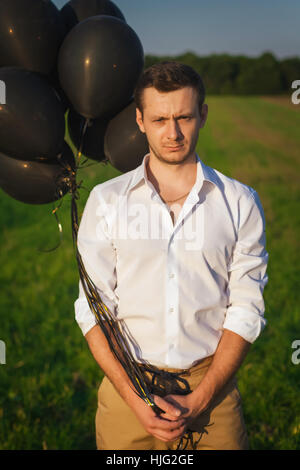 Mann im weißen Hemd mit schwarzen Ballons stehen in einem Feld auf dem Rasen Stockfoto