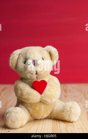 Kleiner Bär halten vorne rot rotes Herz Grunge Hintergrund auf Holztisch. Valentines Konzept. Stockfoto