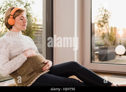 Schwangere Frau sitzen auf Boden, Musik hören Stockfoto