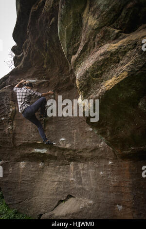 Eine weibliche Kletterer Klettern einen Felsblock ohne Seile, trägt Jeans und ein Hemd. Stockfoto