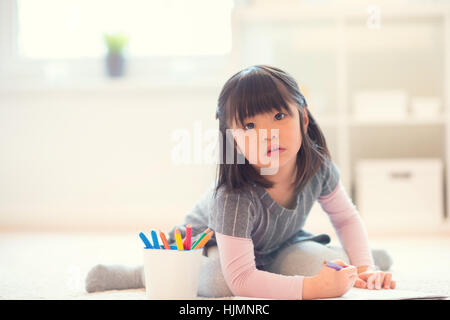 Ziemlich glücklich kleine Japanerin liegend und zeichnen mit Bleistiften auf weißen Capet zu Hause Stockfoto