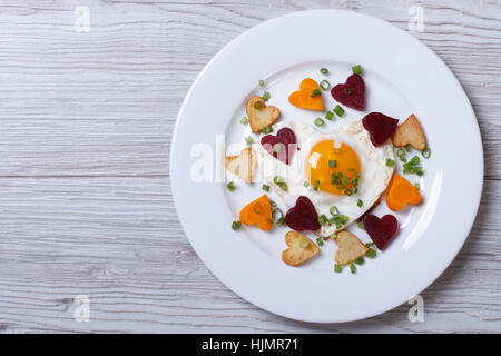 Gebratene Kartoffeln, Karotten, Rüben und Ei in Form von Herzen auf einem Teller. Ansicht von oben. Stockfoto