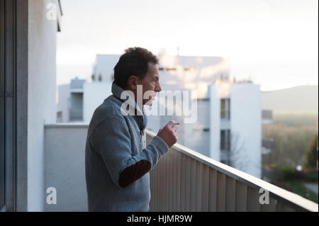 Ernst senior woman auf Balkon stehend, eine Zigarette rauchend Stockfoto