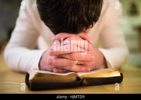 Nicht erkennbare Mann, der betet, kniend auf dem Boden, die Hände auf Bibl Stockfoto