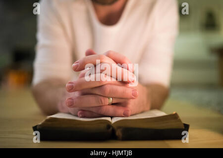 Nicht erkennbare Mann, der betet, kniend auf dem Boden, die Hände auf Bibl Stockfoto