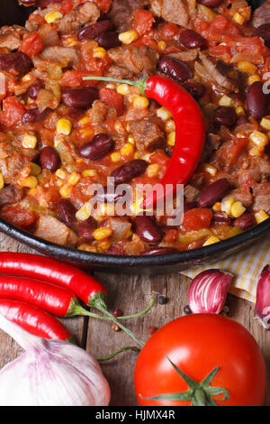 Mexikanisches Chili Con Carne Nahaufnahme in einer Pfanne auf einem hölzernen Hintergrund mit den Zutaten. vertikale Ansicht von oben Stockfoto