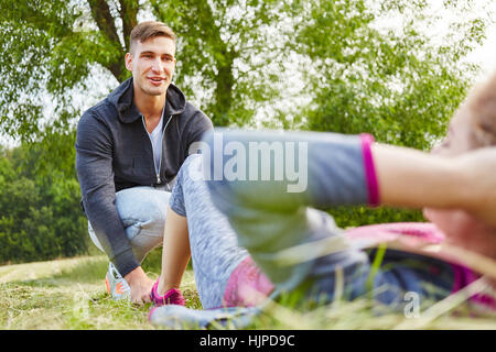 Frau macht Sit-ups während Fitness-Training und Mann hilft ihr Stockfoto